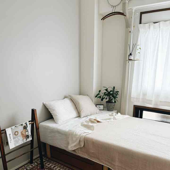 白とベージュのトーンでまとめられた寝室、木製のベッドと寝具、植物が配置された明るくナチュラルなインテリア