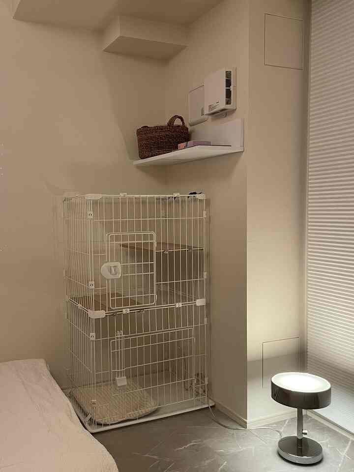 明るいホワイトトーンの寝室の一角、白いキャットケージとシンプルなシルバーフロアランプが配置された空間