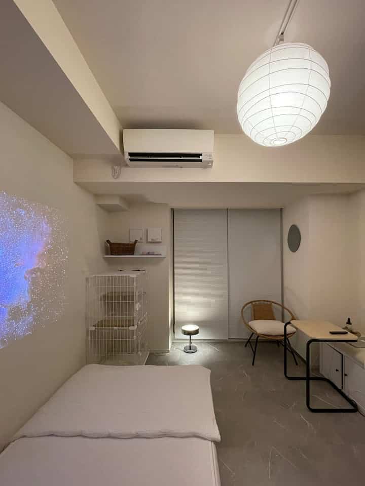 白を基調としたワンルームの寝室、コンパクトな家具とキャットケージが配置されたモダンな空間