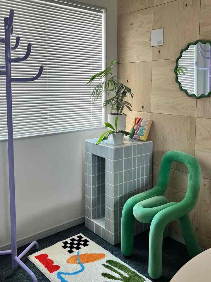 白い壁とブラインド、ナチュラルな木目調パネルにグリーンのアームチェア、植物が置かれたタイルのサイドテーブルが配された印象的なミッドセンチュリーモダン空間