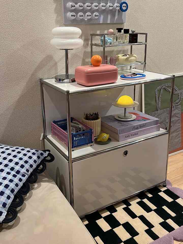 Simple living room space featuring white and pink storage cabinet, black and white patterned rug, and distinctive table lamp