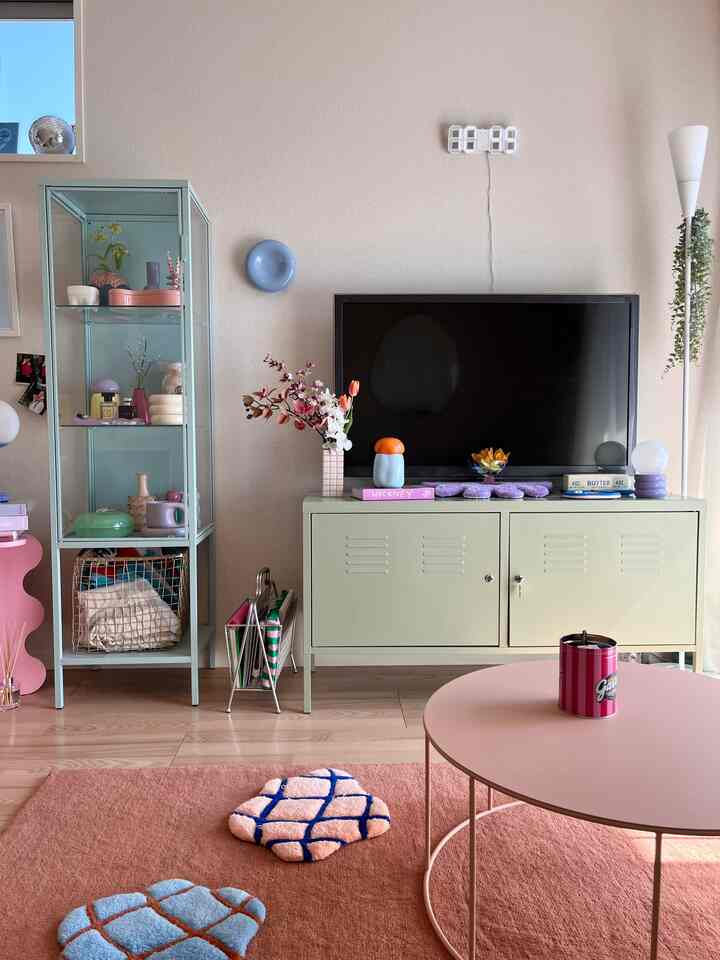 柔らかいトーンのリビング、淡いミントのキャビネットとピンクのコーヒーテーブル、ラグが配置された落ち着いた空間