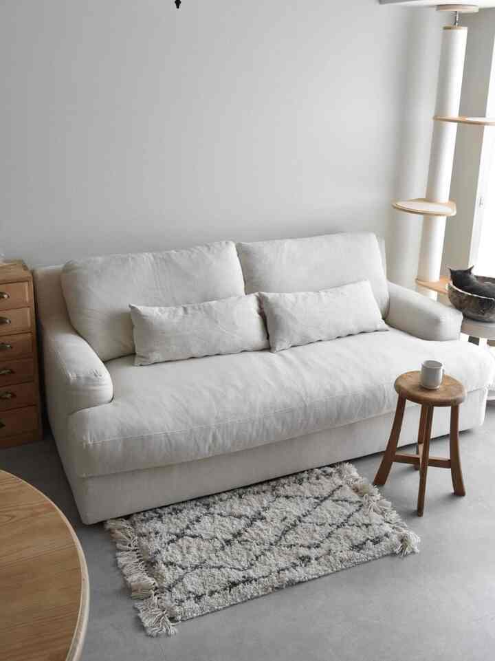 白とナチュラルカラーのリビング、白いソファに木製のスツールとキャットタワーが配置され、落ち着いた雰囲気のある空間