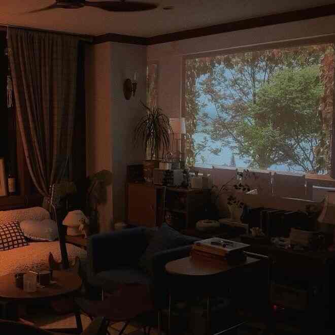 ダークブラウンとブラックのトーンのリビング、ソファと遮光カーテン、プロジェクタースクリーンと植物が配置された雰囲気のあるホームシネマ空間