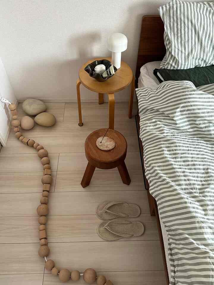 ベージュと木目調のナチュラルモダンな寝室、木製スツールとテーブルランプが配置された雰囲気のある空間