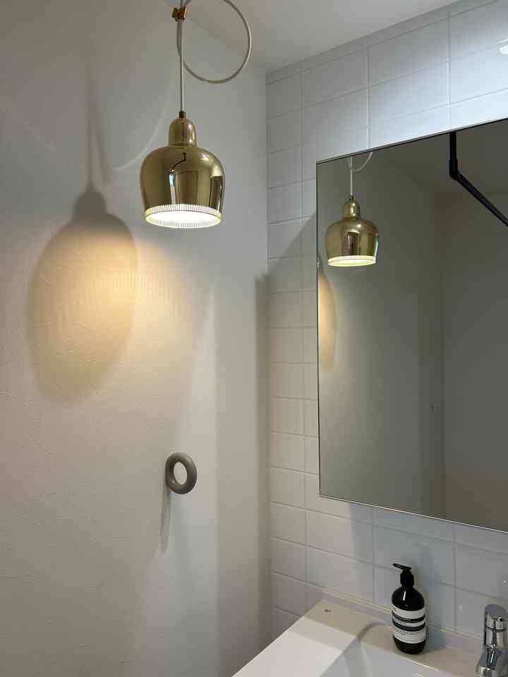 白とゴールドのトーンのバスルーム、ペンダントライトと洗面台が配置されたシンプルなインテリア