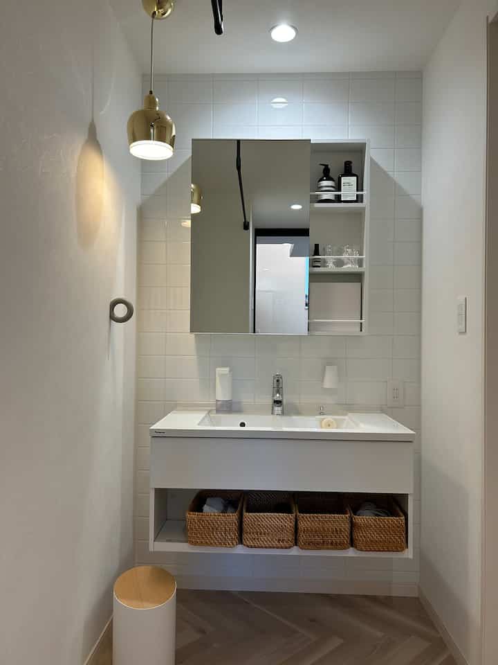 白とナチュラルカラーのバスルーム、ペンダントライトと実用的な収納が配置されたシンプルでモダンなインテリア