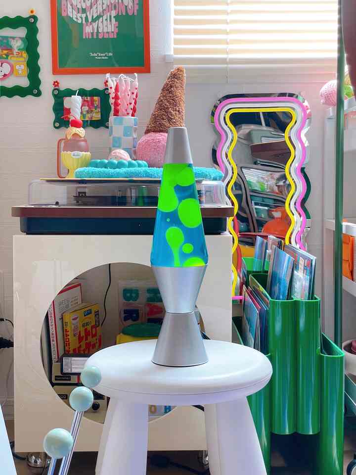 カラフルなレトロスタイルの生活空間、中央に白いスツールの上に置かれた青と緑のラバランプが印象的なインテリア