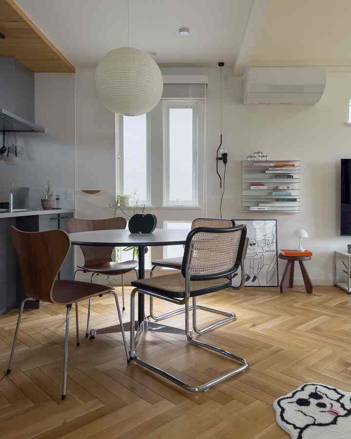 白い壁と木目調の床が特徴のリビングダイニング、丸テーブルと異なる椅子が配置されたモダンでスカンジナビア風の印象的な空間