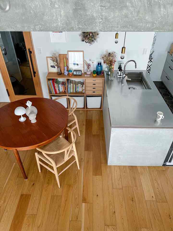 ナチュラルな木目調と白い壁のリビング・キッチン空間、丸いダイニングテーブルとウィッシュボーンチェアが配置された温かみのあるインテリア