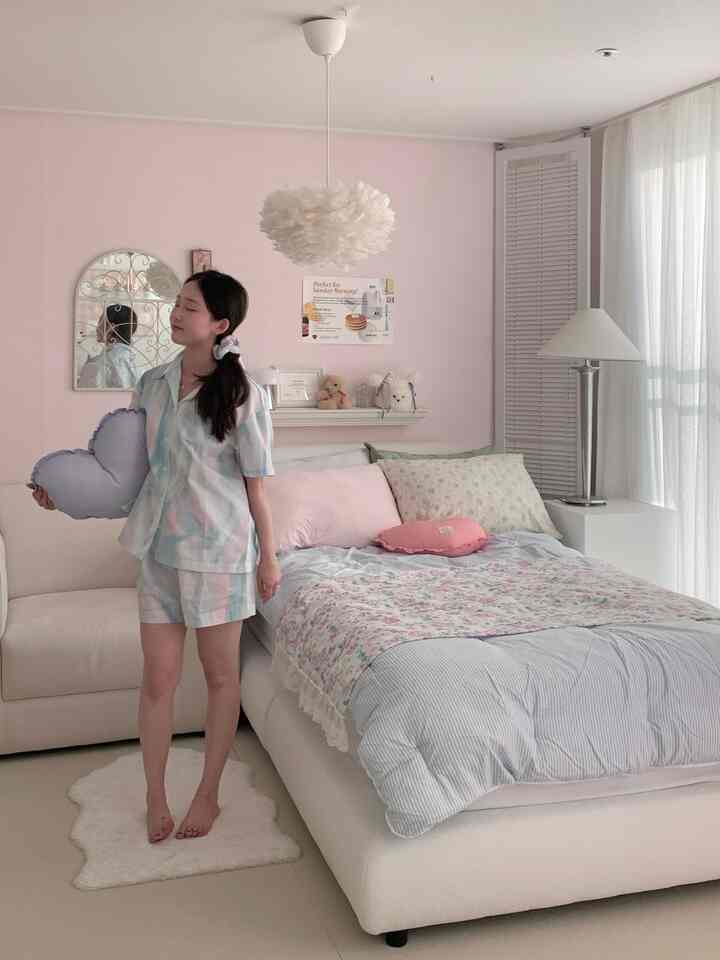 パステルピンクの壁と白いベッド、柔らかなファブリックソファが配置された温かみのある寝室