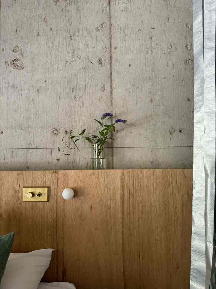 Natural brown wood and gray concrete wall hotel-like bedroom featuring a transparent vase with greenery