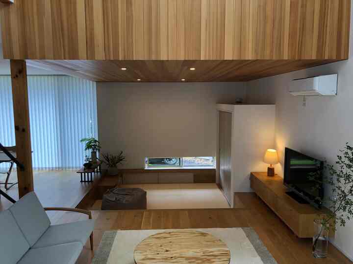 ナチュラルな木目調のリビング、低い天井とソファ、丸いテーブルが配置された落ち着いた雰囲気のインテリア