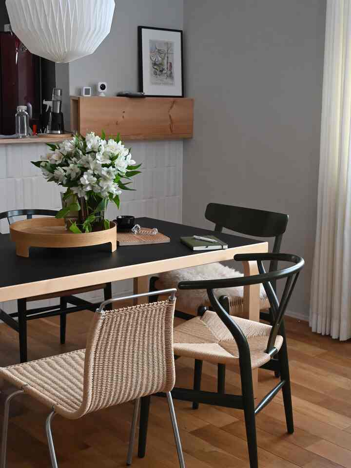 ナチュラルな木目調と黒を基調とした北欧スタイルのダイニングルーム、様々な椅子が並ぶテーブル中央にアルストロメリアの花瓶が配置された印象的な空間