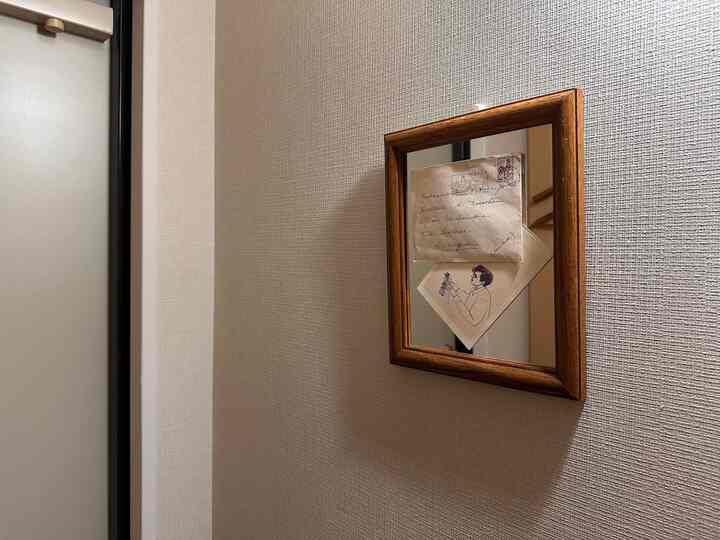 ベージュ色の壁と木枠の鏡が配置された狭い玄関の印象的な空間