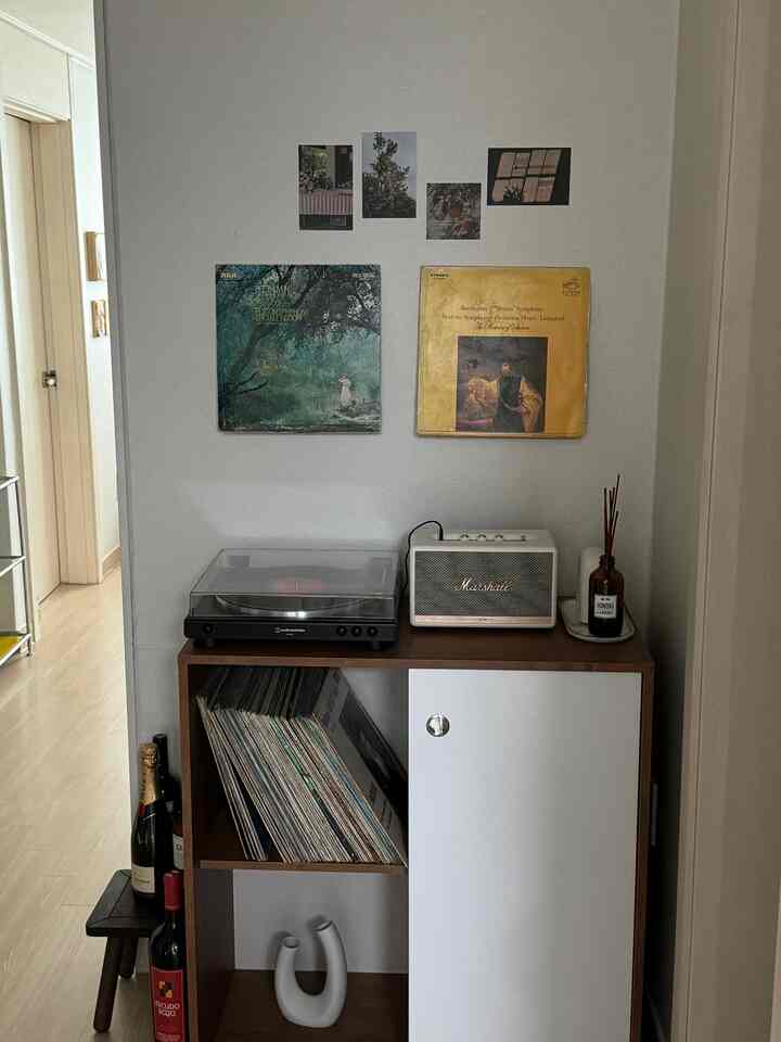 ナチュラルトーンのリビングルームの一角に、ターンテーブルとマーシャルスピーカーが置かれた木製収納棚とヴィンテージLPレコードが配置された印象的な空間。