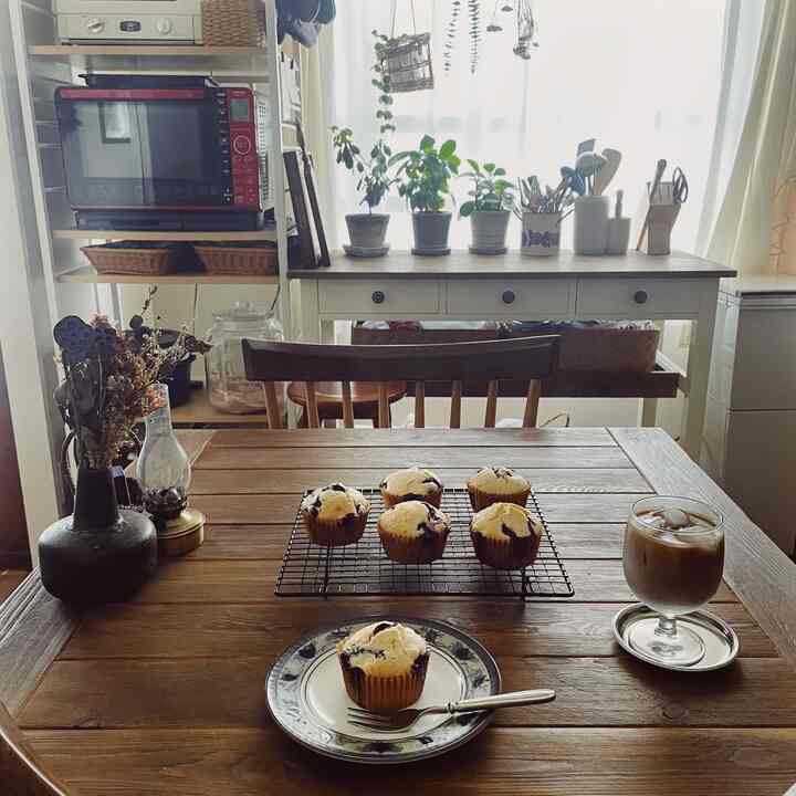 ナチュラルな木目調のキッチンとダイニングスペース、おうちカフェの雰囲気を感じるブルーベリーマフィンとアイスコーヒーが置かれた印象的な空間