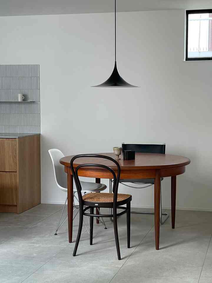 白い壁と木製の丸いダイニングテーブル、多様なデザインの椅子が配置されたモダンでシンプルなダイニング空間