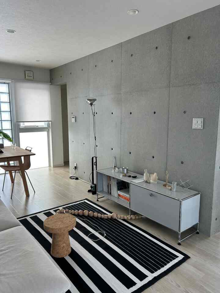 白とナチュラルカラーの調和が取れたリビング、コルクのサイドテーブルとモダンなコンクリート壁が印象的な空間