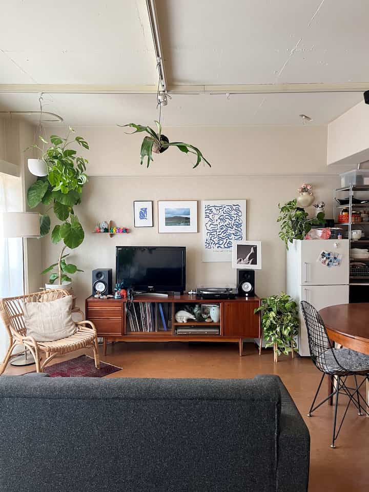 ナチュラルな色調のワンルームリビング、ヴィンテージ家具と多様な植物が配置された温かみのある空間