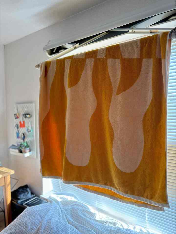 明るい黄色のタオルが掛かった一人暮らしの寝室、自然な木製家具と整った寝具が配置された空間