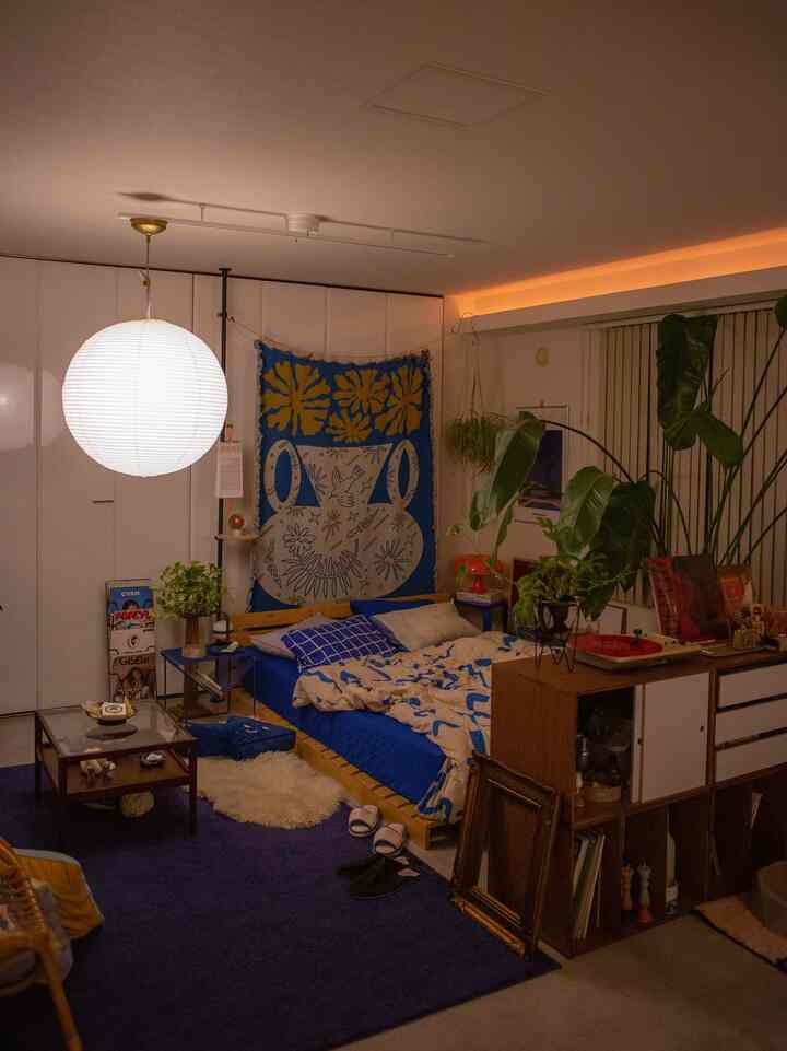 Natural modern bedroom featuring blue bedding and warm orange lighting, with plants and storage creating a cozy atmosphere