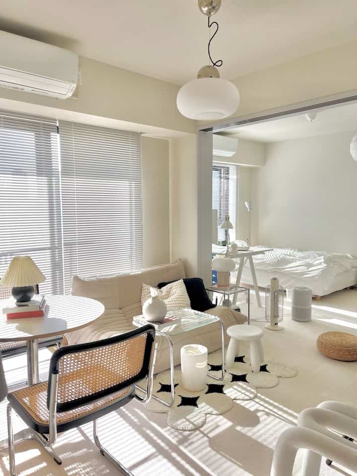 明るい白とベージュの色調の二人暮らし用寝室とリビング、ブラインドから朝日が差し込むナチュラルモダンな雰囲気のインテリア