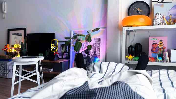A small bedroom with white walls and striped bedding featuring neon lighting and various decorative objets in a natural, simple atmosphere