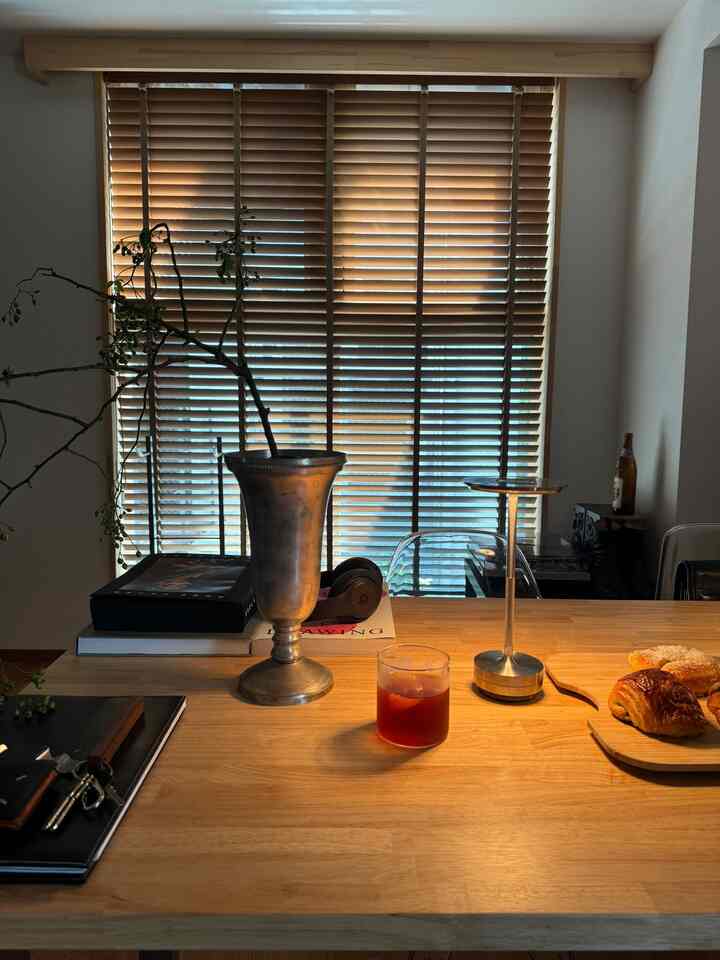 木目調のテーブルとウッドブラインドが配された温かみのあるダイニング、アイスコーヒーとクロワッサンが置かれた空間