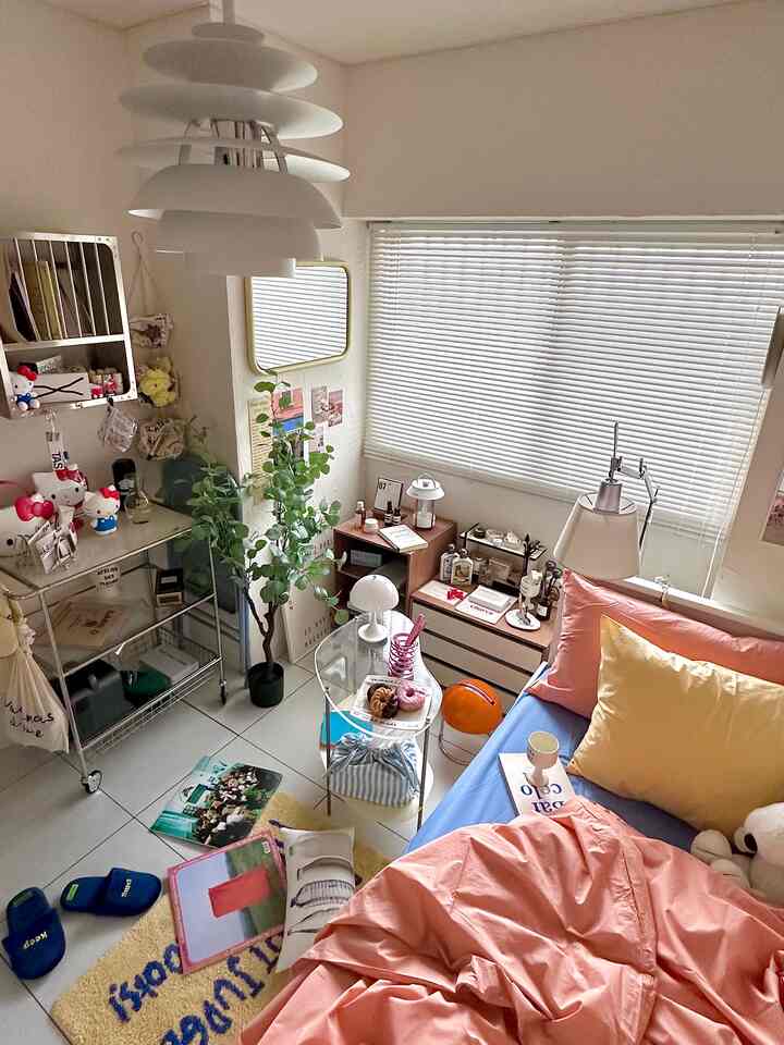 白い壁とブラインド、パステルピンクと黄色の寝具が配置された温かみのある寝室