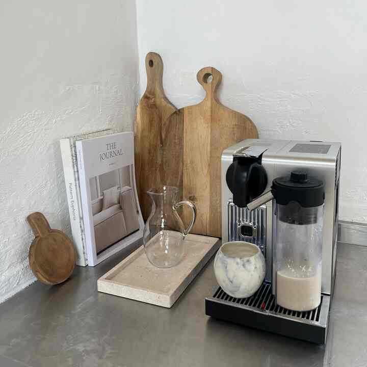 ナチュラルな色調のキッチンコーナーに、コーヒーマシン、木製のまな板、大理石のトレイが整然と配置された雰囲気のあるインテリア