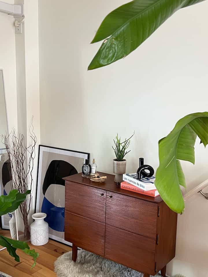 白い壁と茶色のヴィンテージキャビネットが配置されたナチュラルなリビング、ポスターと植物が調和する雰囲気のあるインテリア