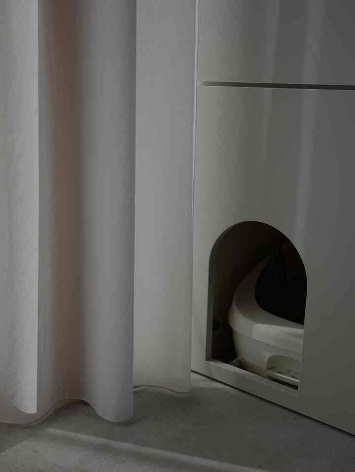 白を基調とした玄関のシューズラック内に設置された猫トイレとレースカーテンが配置された雰囲気のある空間