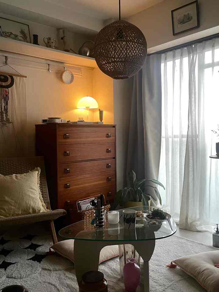 ナチュラルブラウンとベージュのカーテンがある1人暮らし向け1Kのリビング、ラタンバスケットとガラステーブルが配置された落ち着いた空間