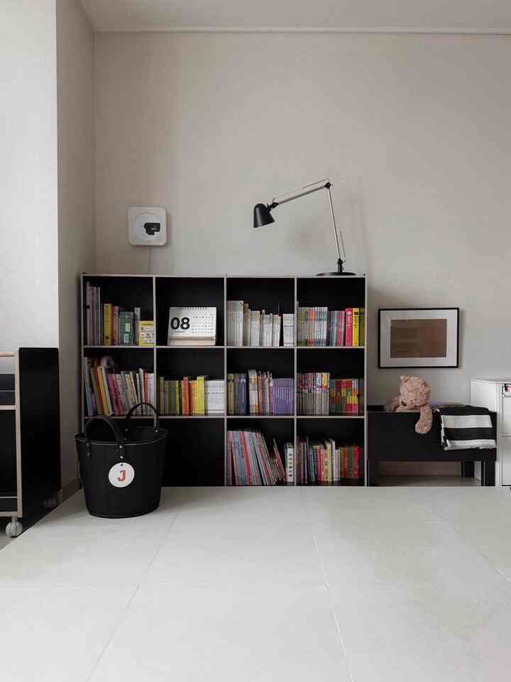 White walls and floor with black bookshelf and table lamp in a living room for a household living with a baby
