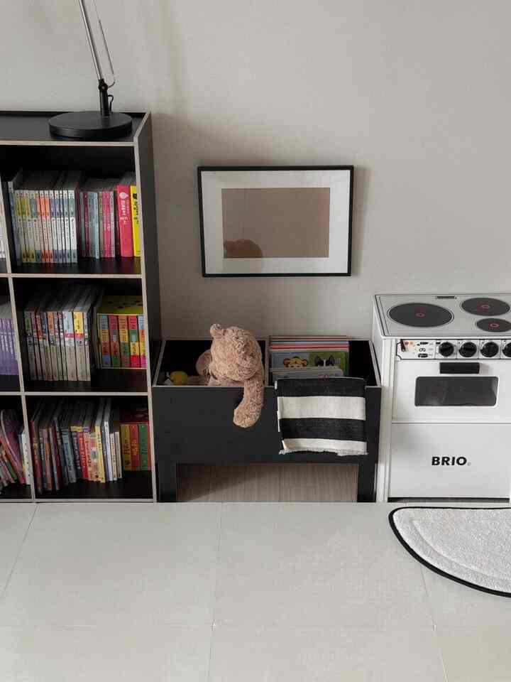 Modern kids' room featuring a black bookshelf, toy storage, and wooden play kitchen with a calm atmosphere