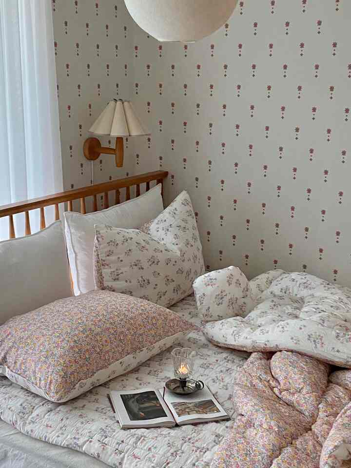 A white and wood-tone bedroom featuring floral patterned bedding and wall sconce, creating a cozy atmosphere