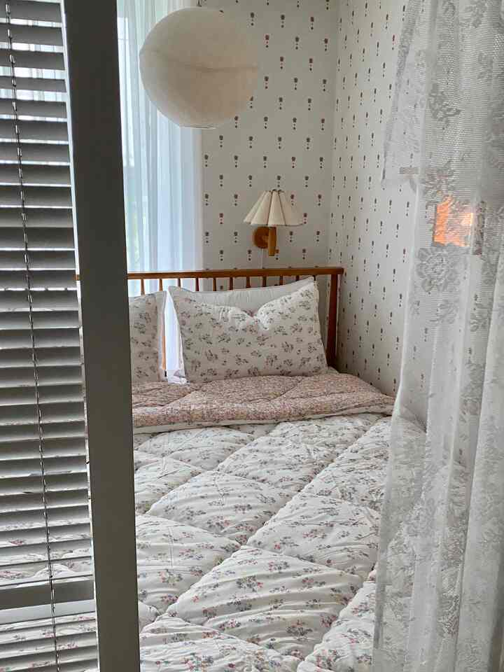 白を基調とした空間にブラウンの木製ベッドとフレンチフラワー柄の寝具が配置された温かみのある寝室