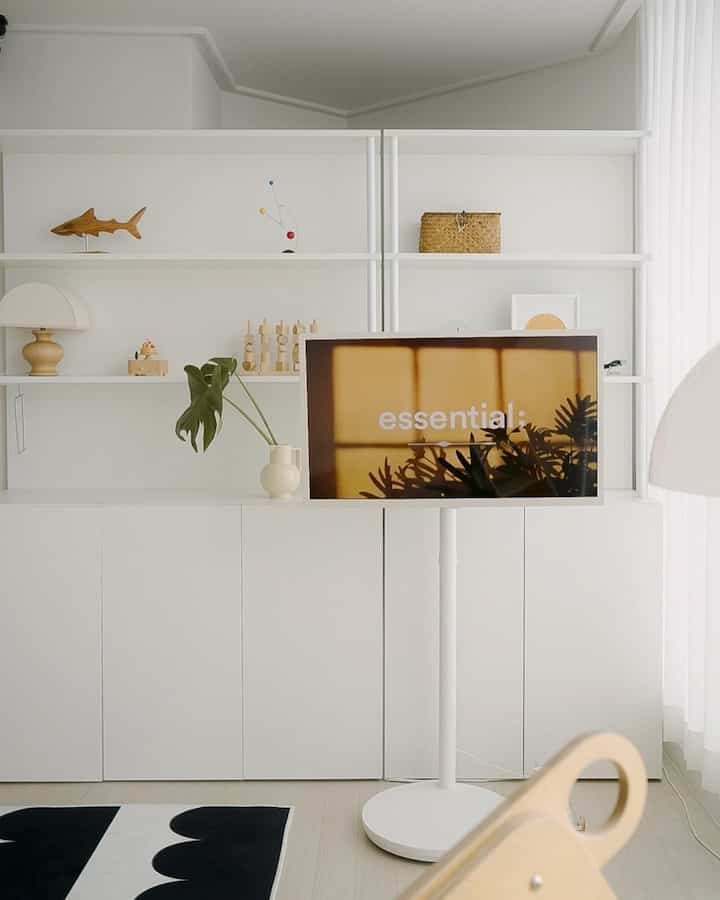 明るいホワイトとナチュラルウッド調のリビング、中央にスタンド型テレビと白黒のラグが配置されたシンプルモダンな空間