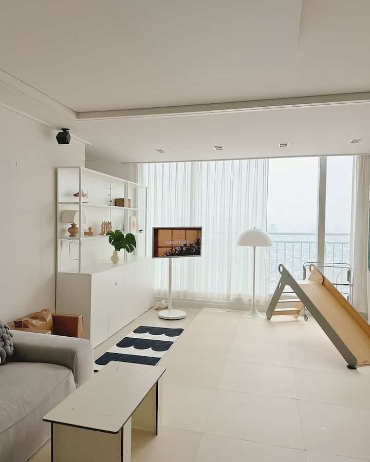 Bright white-toned living room featuring a kids' slide, monitor stand, and floor lamp in a modern, clean interior