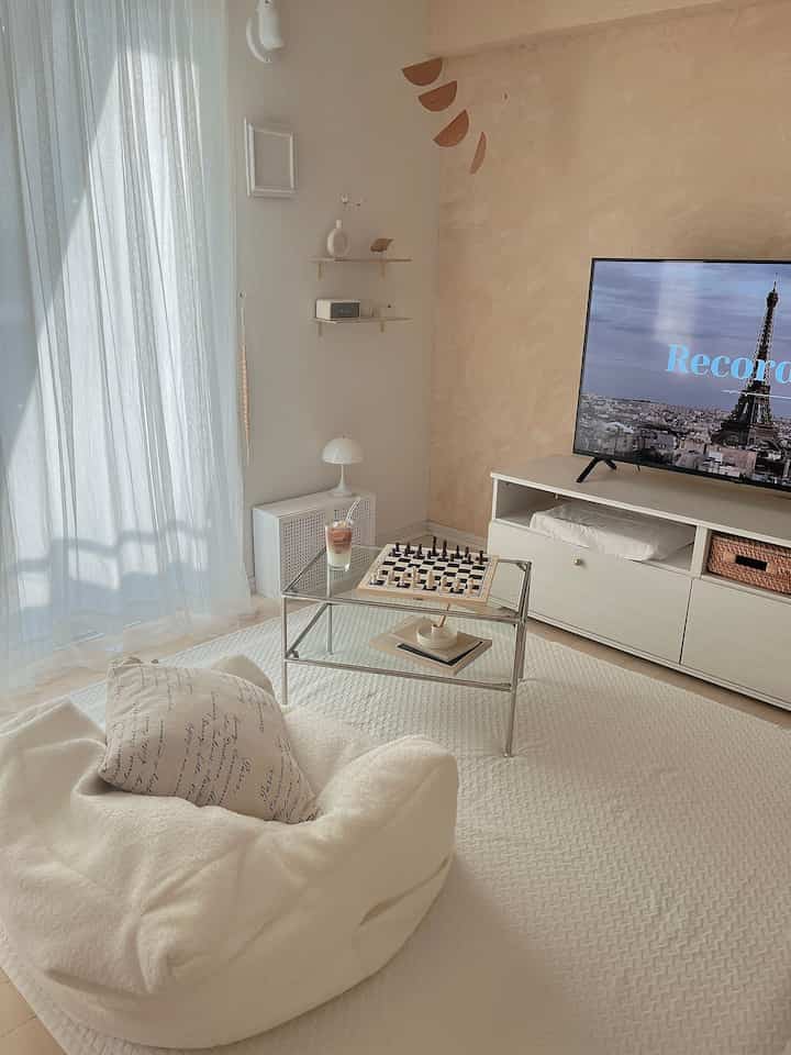 Bright white and light beige living room featuring a transparent sofa table with chess set, simple and cozy atmosphere