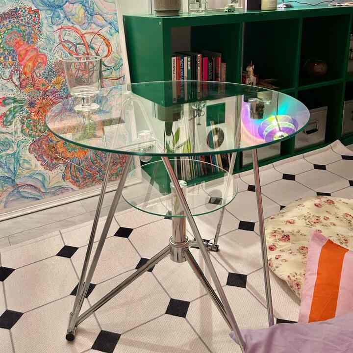 Transparent glass table with green bookshelf on a monotone patterned rug in a cozy living room space