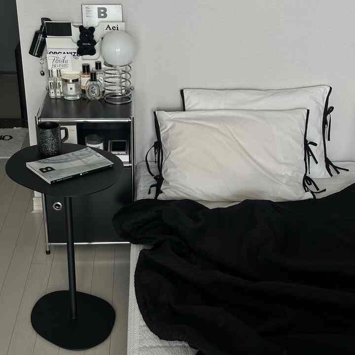 Simple modern bedroom featuring white walls and bedding with black accent side table and blanket