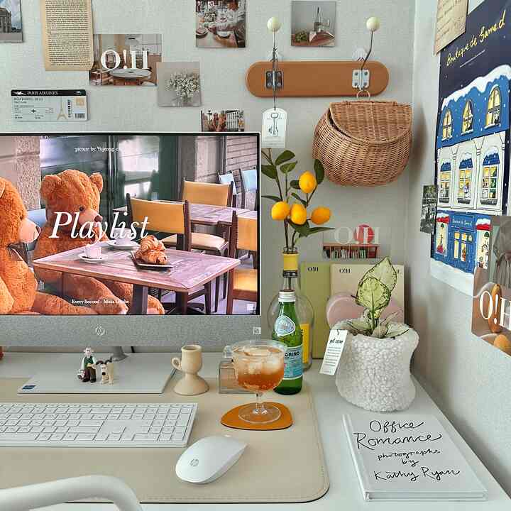 White and beige toned home office space featuring all-in-one PC, plants, and posters with cozy desk setup for living with a baby