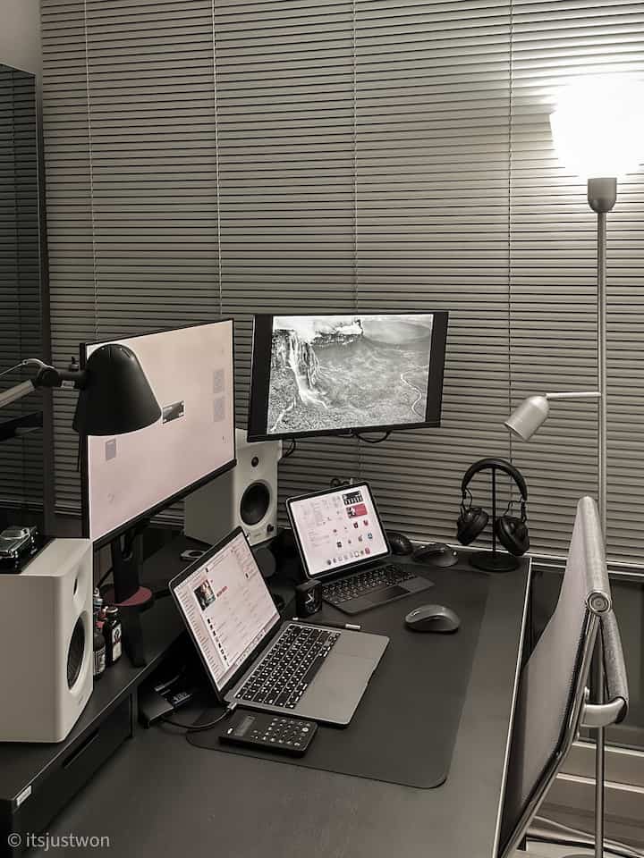 Monotone black and silver Mid-Century Modern home office featuring a sleek desk with dual monitors, MacBook, and mesh office chair