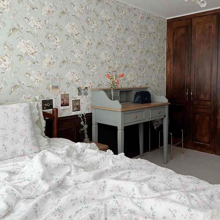 A softly toned bedroom with floral patterned wallpaper, wood-toned furniture, and vintage ambiance