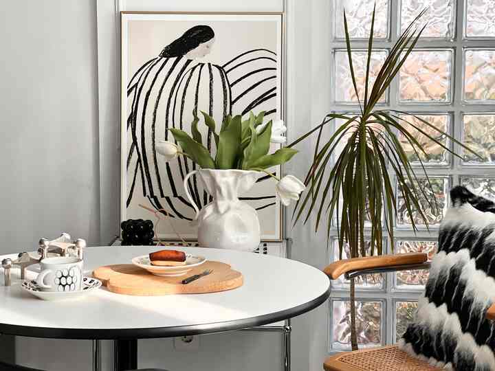 Modern dining space in white and wood tones featuring a white vase with tulips and green plants, creating a cozy cafe style interior