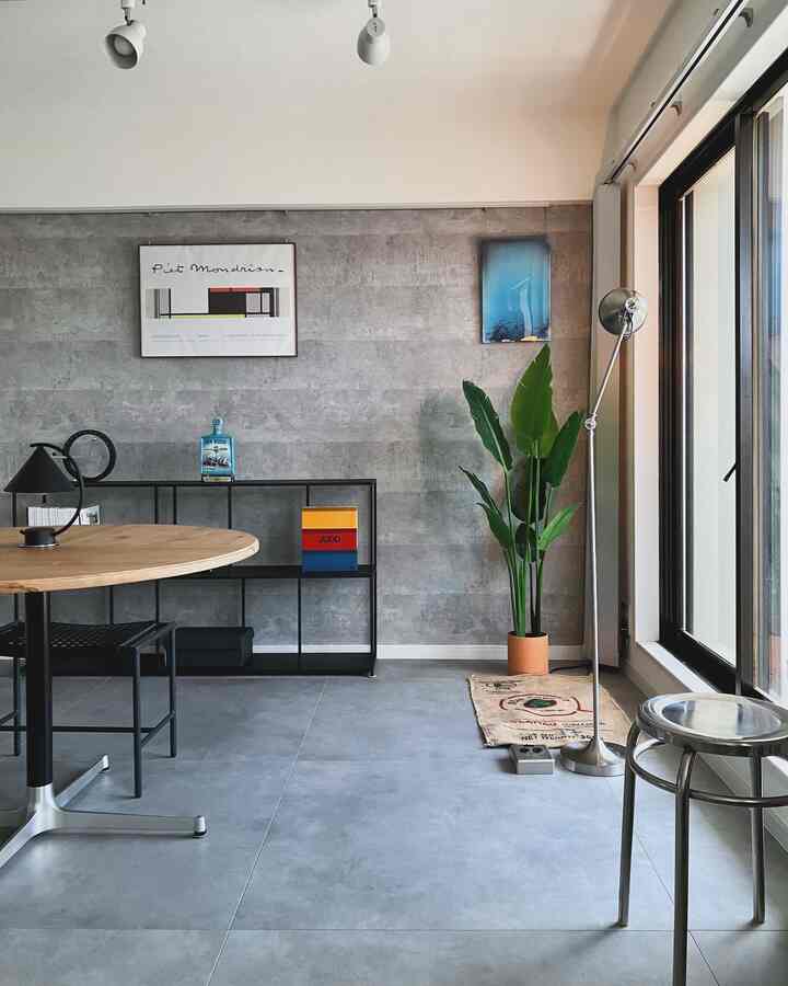 グレーの壁面と木目調の丸いダイニングテーブル、インダストリアルスタイルのフロアランプと緑の植物が配置されたモダンなリビング空間