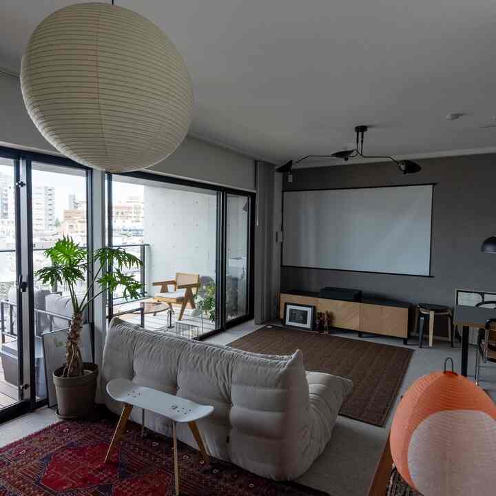 明るい白を基調としたリビング、低めのホワイトトゴソファと木製テレビ台、大型ペンダントライトとプロジェクタースクリーンが配置されたモダンでナチュラルな空間