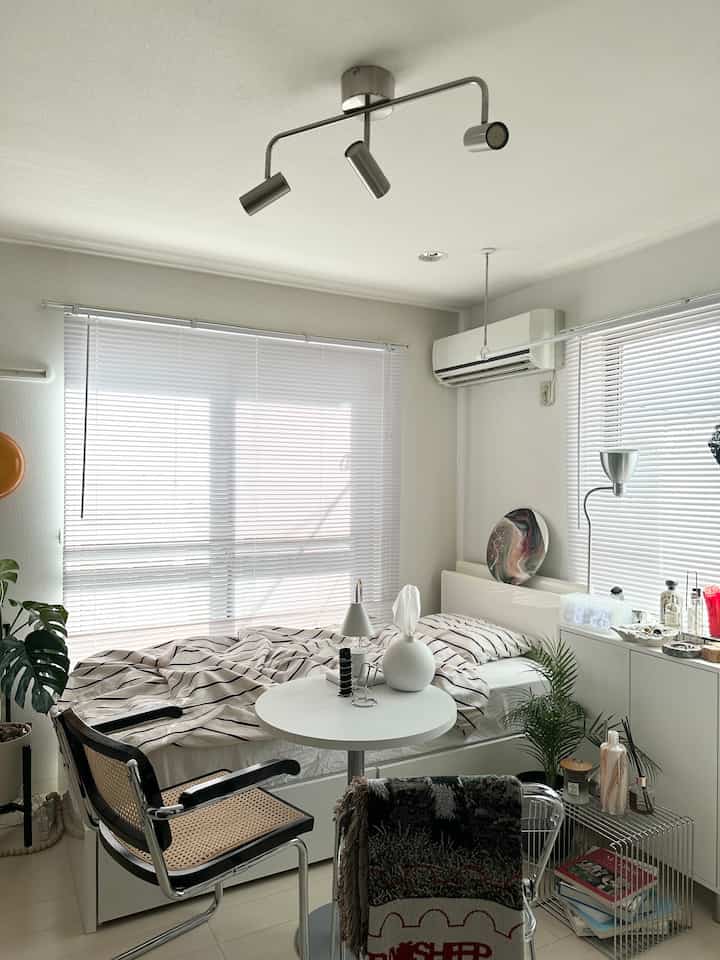 ホワイトトーンの8畳ワンルーム寝室、ラタンチェアとラウンドテーブルが配置されたナチュラルな雰囲気のインテリア